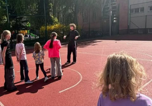 Trenerka tłumaczy dzieciom zasady nowej zabawy sportowej.