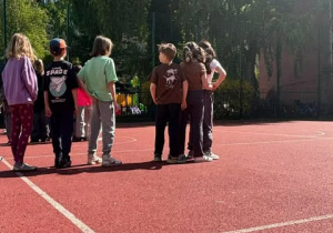 Dzieci stoją na boisku czekając na kolejną zabawę sportową.