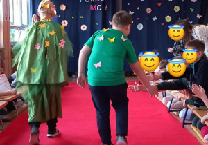 Chłopcy prezentują zielone stroje z kolorowymi motylkami na wybiegu.