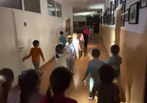 Nocne zwiedzanie szkoły, dzeci idą szkolnym korytarzem.