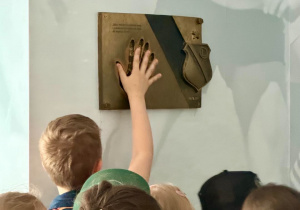 Chłopiec przykłada rękę do odcisku dłoni pana Lucjana Brychczego.